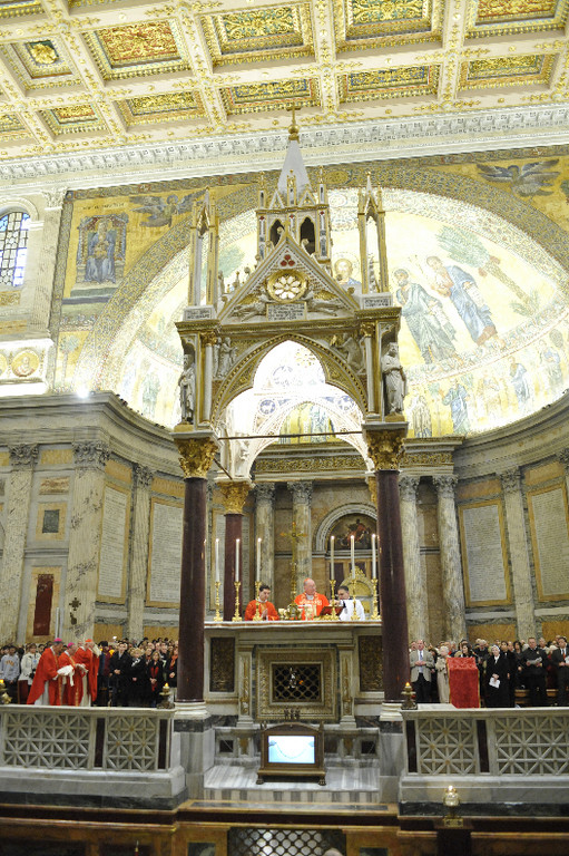 Cardinal Dolan elevates the Eucharist during the final Mass of the pilgrimage to Rome at the Basilica of St. Paul Outside the Walls Feb. 20. With him at the altar is Cardinal Egan, Archbishop Emeritus of New York and a fellow member of the College of Cardinals. Overall view at left shows concelebrating bishops and pilgrims.