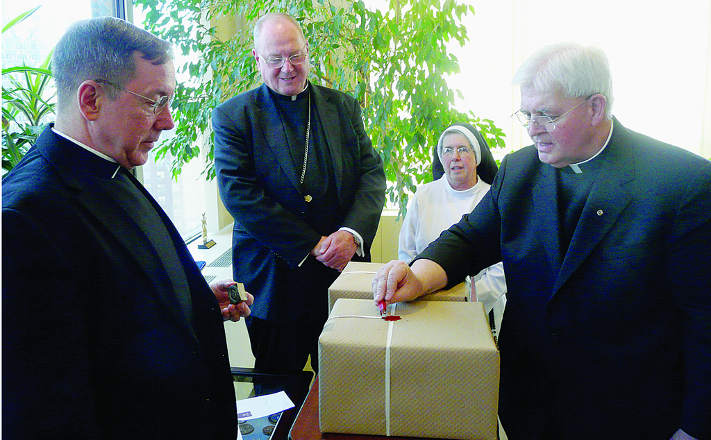 SEALED FOR DELIVERY—Father Gabriel O’Donnell, O.P., postulator for the sainthood cause of Rose Hawthorne Lathrop, seals packages of documents to be submitted to the Congregation for the Causes of Saints in Rome to support her canonization. At left is Msgr. Douglas Mathers, vice chancellor of the archdiocese. Cardinal Dolan looks on with Mother Mary Francis Lepore, O.P., superior general of the Dominican Sisters of Hawthorne, the order Rose Hawthorne Lathrop founded.