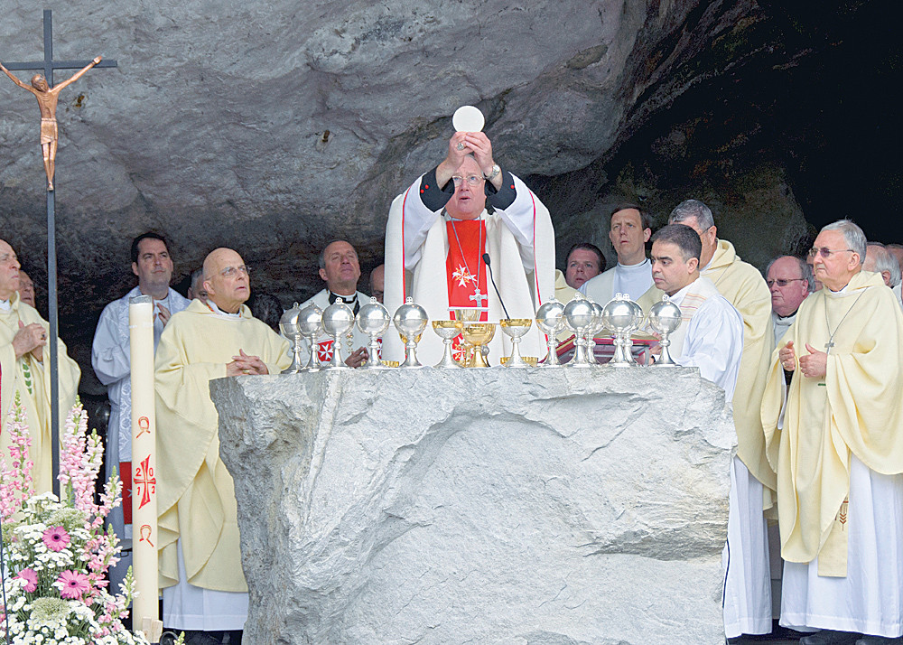 CONSECRATION—Cardinal Dolan elevates the Eucharist during a Mass he offered in the Grotto at Lourdes in France during an annual pilgrimage of the Order of Malta this month. Next to the Paschal Candle is Cardinal Francis George of Chicago.