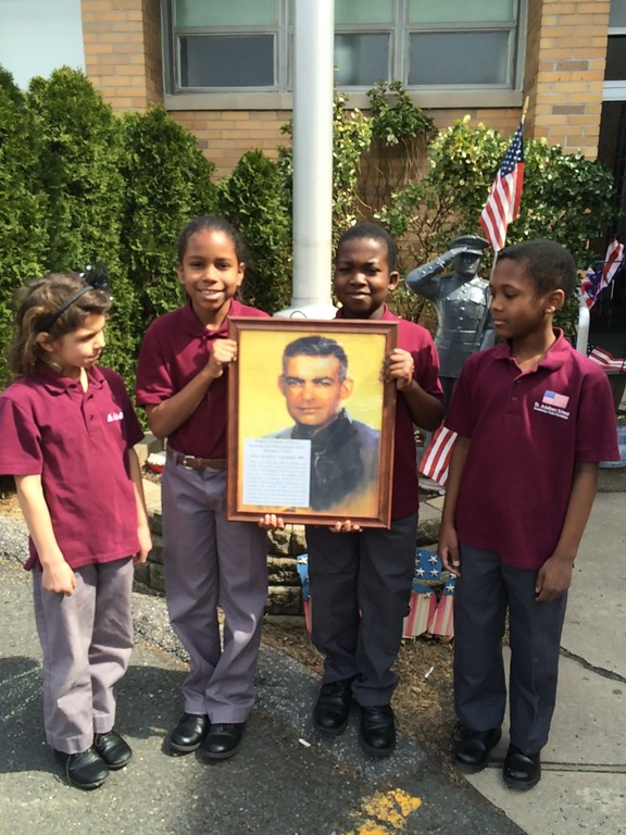 St. Adalbert students Victoria Walter, Ariel Gonzalez, Musa Donzo and Seth Wiltshire hold a photo of Father Vincent Capodanno, M.M., a Navy chaplain and Staten Island native who was killed during the Vietnam War, before the morning bell earlier this school year. The children pray each morning for his sainthood cause.