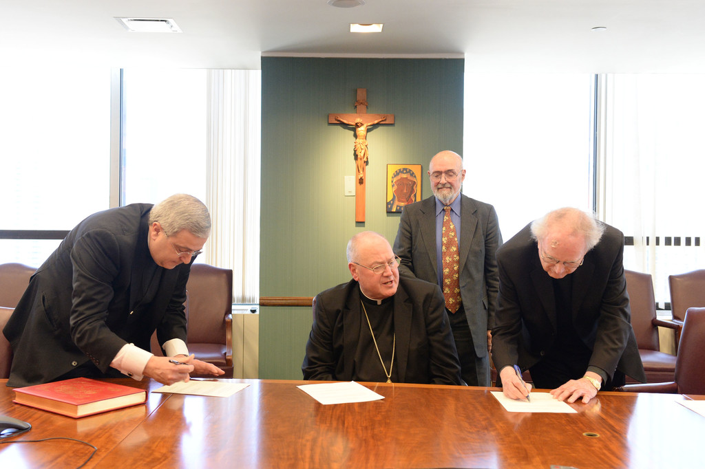Father Richard L. Welch, C.Ss.R., promoter of justice, at far left, and Father Raymond M. Rafferty, the archbishop’s delegate, sign documents at the ceremony in which Cardinal Dolan opened the canonical inquiry into the life of Dorothy Day April 19 at the New York Catholic Center. Looking on are the cardinal and George B. Horton, liaison for the Dorothy Day Guild.