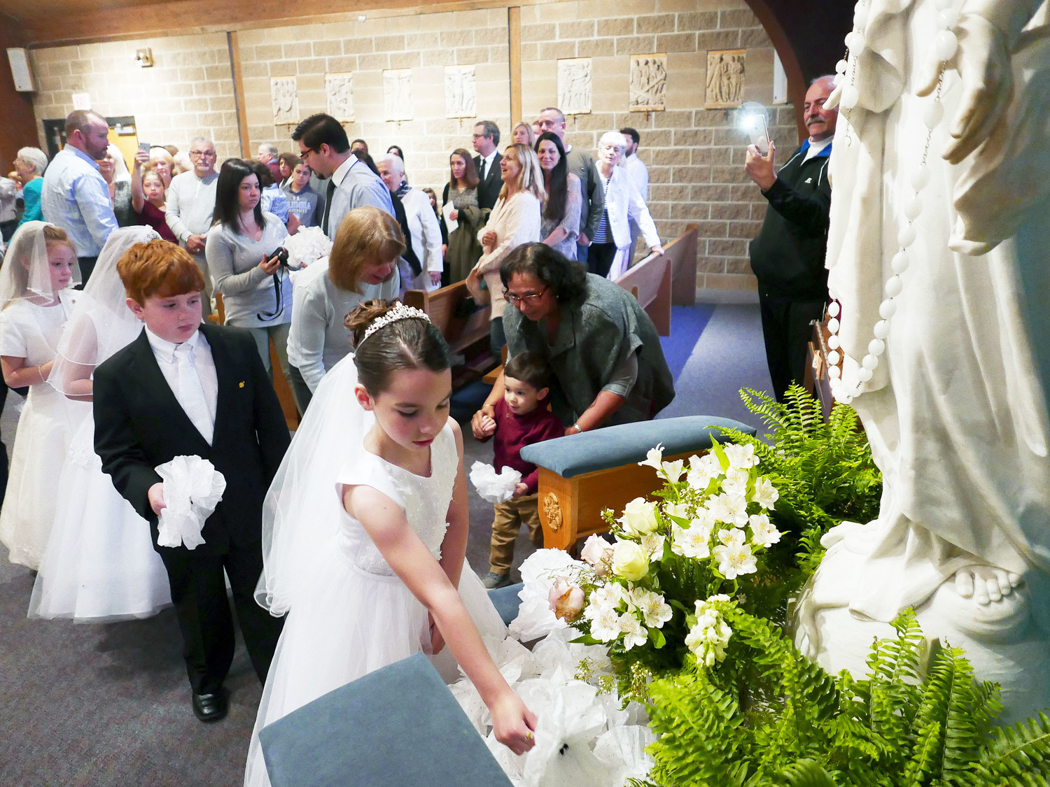Kayleigh Mahoney, who along with her classmates received the sacrament of First Holy Communion May 5, places a flower at the base of a statue of the Blessed Mother at Immaculate Conception Church in Stony Point during a May Crowning ceremony on Mothers’ Day, May 13.