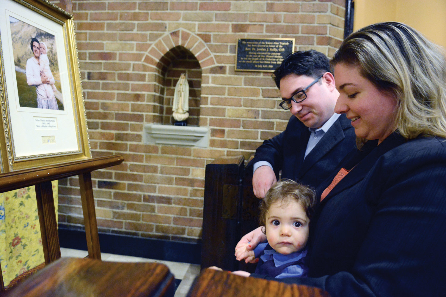 Jason and Carrie Caminiti kneel with their 14-month-old son Christian during veneration in front of a framed photo and relic of St. Gianna Beretta Molla at St. Catherine of Siena Church in Manhattan May 16.