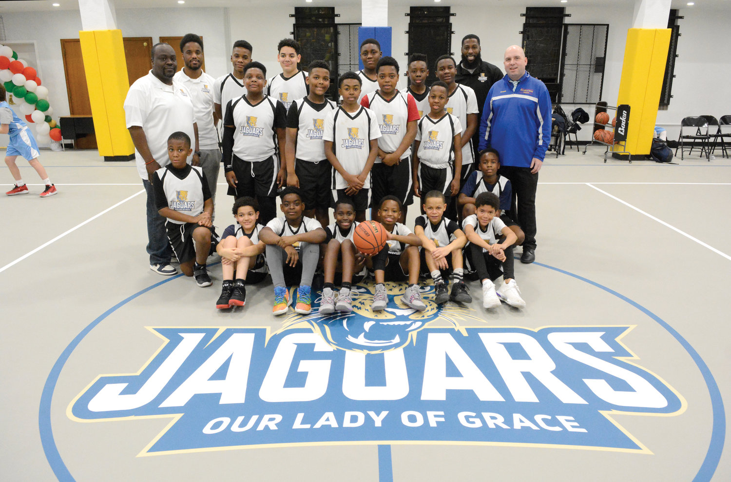 TEAMWORK—Coaches and players from the fifth- and sixth-grade and seventh- and eighth-grade boys’ teams at Our Lady of Grace School in the Bronx gather around the school’s Jaguars logo at center court with principal Rich Helmrich, far right, in the school’s new gymnasium in the Bronx Jan. 8.