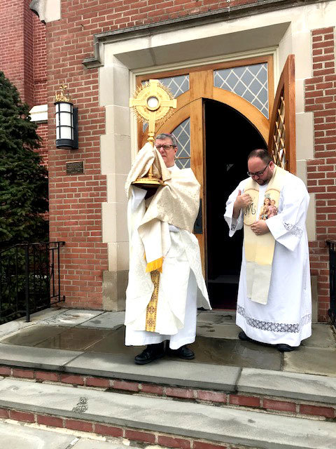 BLESS AND PROTECT—Auxiliary Bishop Gerardo Colacicco, episcopal vicar for the Northern counties of the archdiocese, holds a monstrance containing the Blessed Sacrament outside the front door of St. Mary’s Church in Wappingers Falls March 19, the feast of St. Joseph. At right is Father Justin Cinnante, O. Carm., making the sign of the cross. Bishop Colacicco, who is a priest in residence at St. Mary’s, had requested pastors of Dutchess, Orange, Ulster and Sullivan counties also offer a simple Benediction with the Blessed Sacrament outside the front door of their churches at noon that day, invoking the blessing and protection of all their people against the spread of the coronavirus. “Let our intention be the same: to seek God’s mercy and forgiveness, to ask for Holy protection from the spread of the coronavirus and an end to this pandemic,” he said in an email to them. “How powerful a sign it will be if we all do this on the same day and at the same time. Even though our people cannot gather to be present, it is our hope that it will bring them comfort knowing that this was done by their priests.”