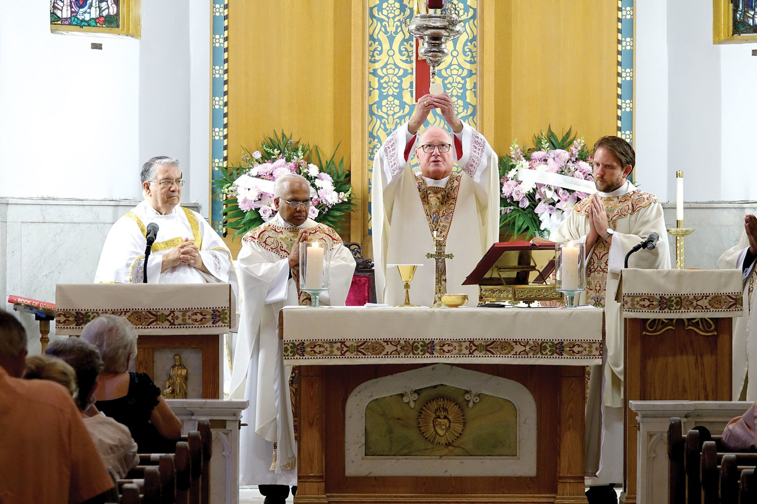 Cardinal Dolan elevates the Eucharist during Mass. At the altar are Deacon Anthony Viola, far left, of Immaculate Conception and Assumption of Our Lady parish, Tuckahoe; Father Joseph Emmanuel, pastor of St. Joan of Arc-Our Lady of Mount Carmel; and Father Stephen Ries, right, priest secretary to Cardinal Dolan.