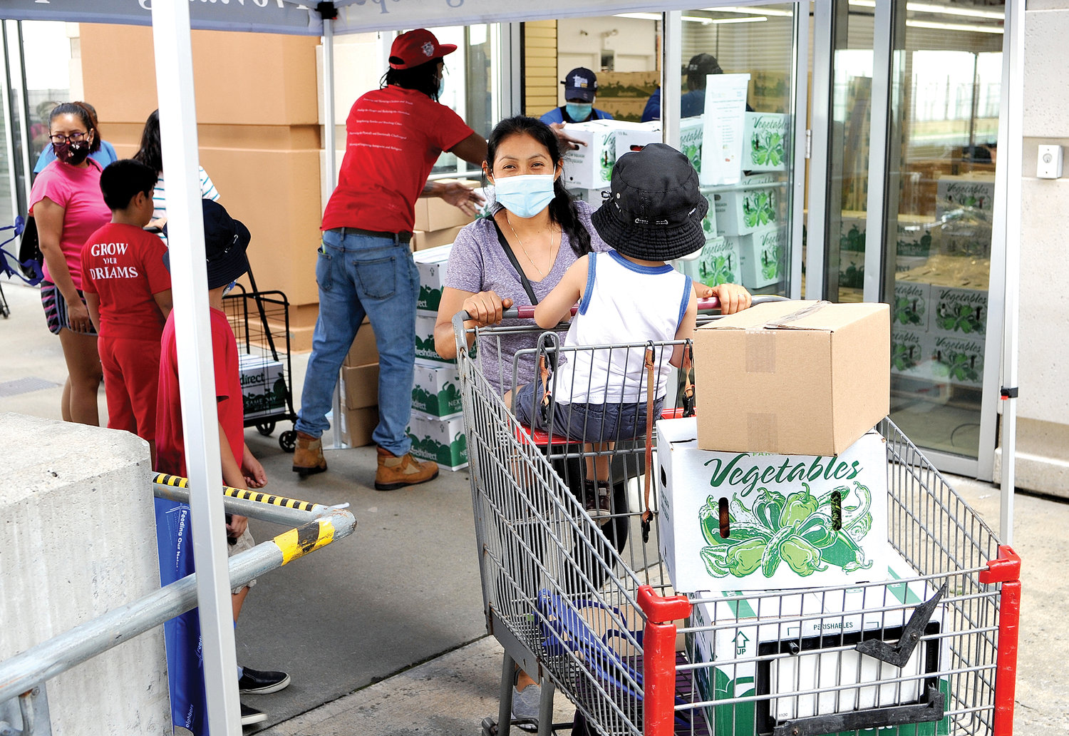 A woman with a young child smiles behind her mask as she fills her cart at the event where 1,000 bags of food and produce and 1,000 gallons of milk were distributed.