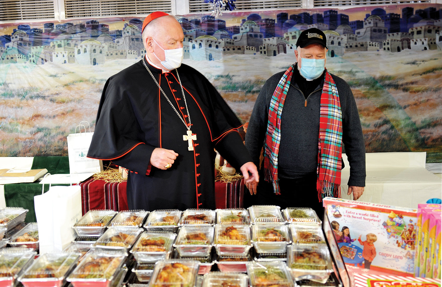 At Abraham House Dec. 22 in the Mott Haven section of the Bronx, Cardinal Dolan and Msgr. Kevin Sullivan, executive director of archdiocesan Catholic Charities, stand near the food provided through Abraham House, an affiliate of Catholic Charities.