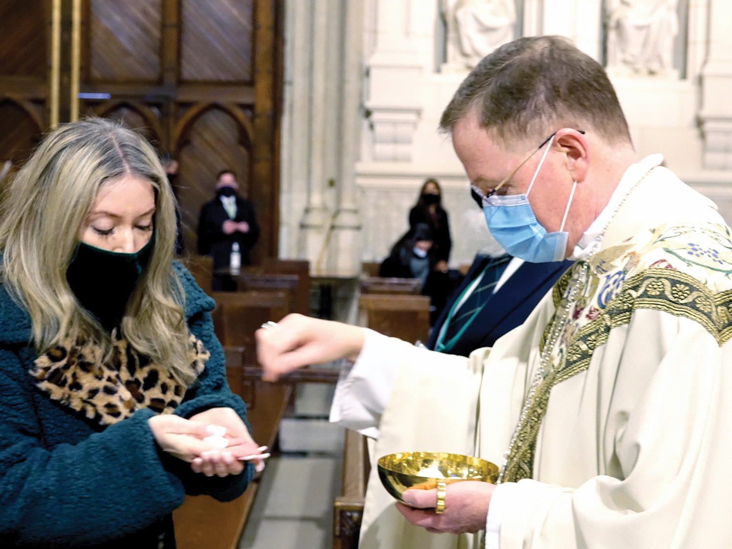 Auxiliary Bishop Edmund Whalen distributes the Eucharist during the morning liturgy. The bishop was cited as part of the parade’s first-ever honor guard of first responders and essential workers.
