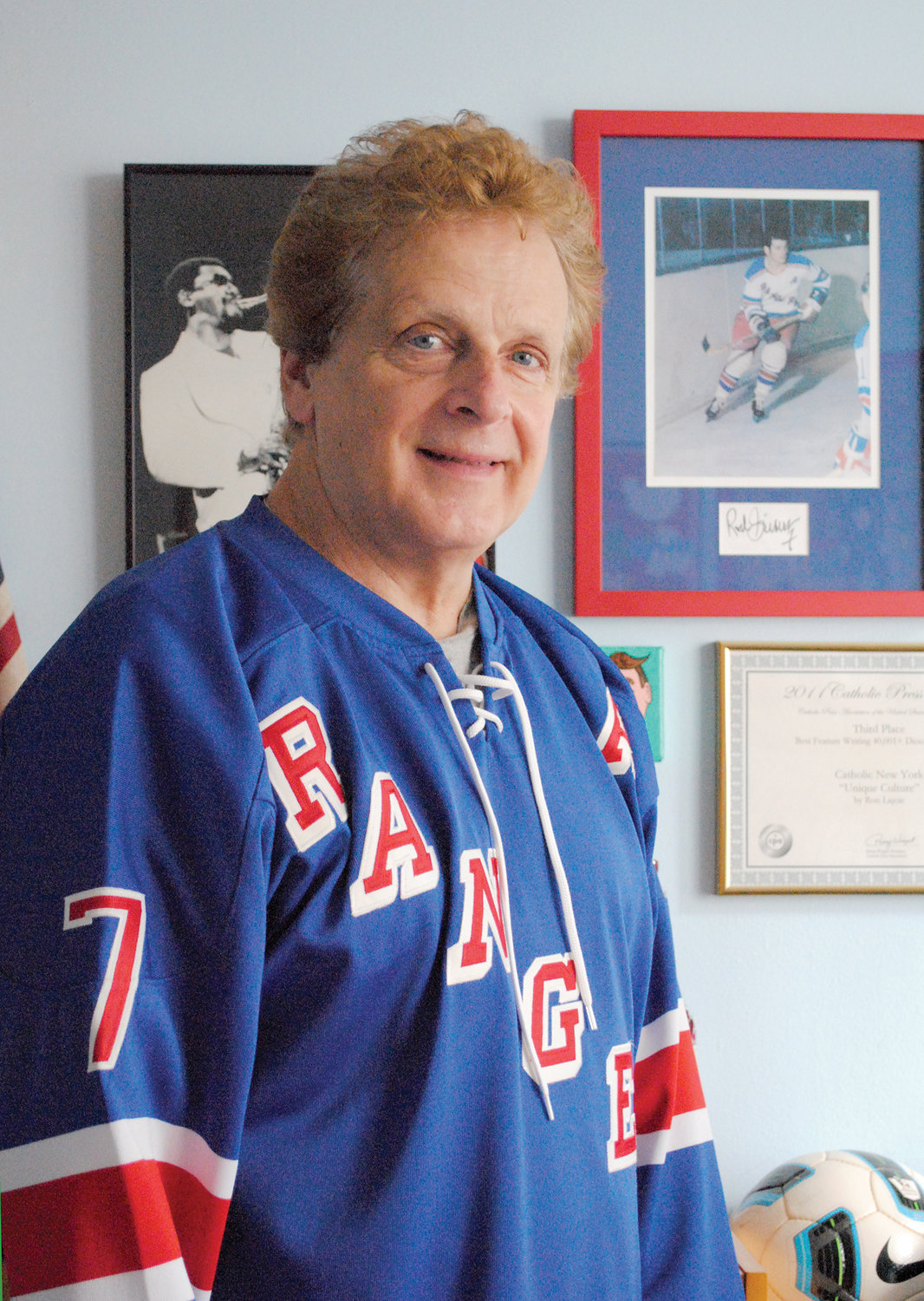 Former Catholic New York reporter Ron Lajoie wears his No. 7 Rod Gilbert wool jersey in front of a framed photo of the Ranger great at his home in Manhattan. Gilbert, the Rangers all-time leader in goals and points, died Aug. 19 at age 80.