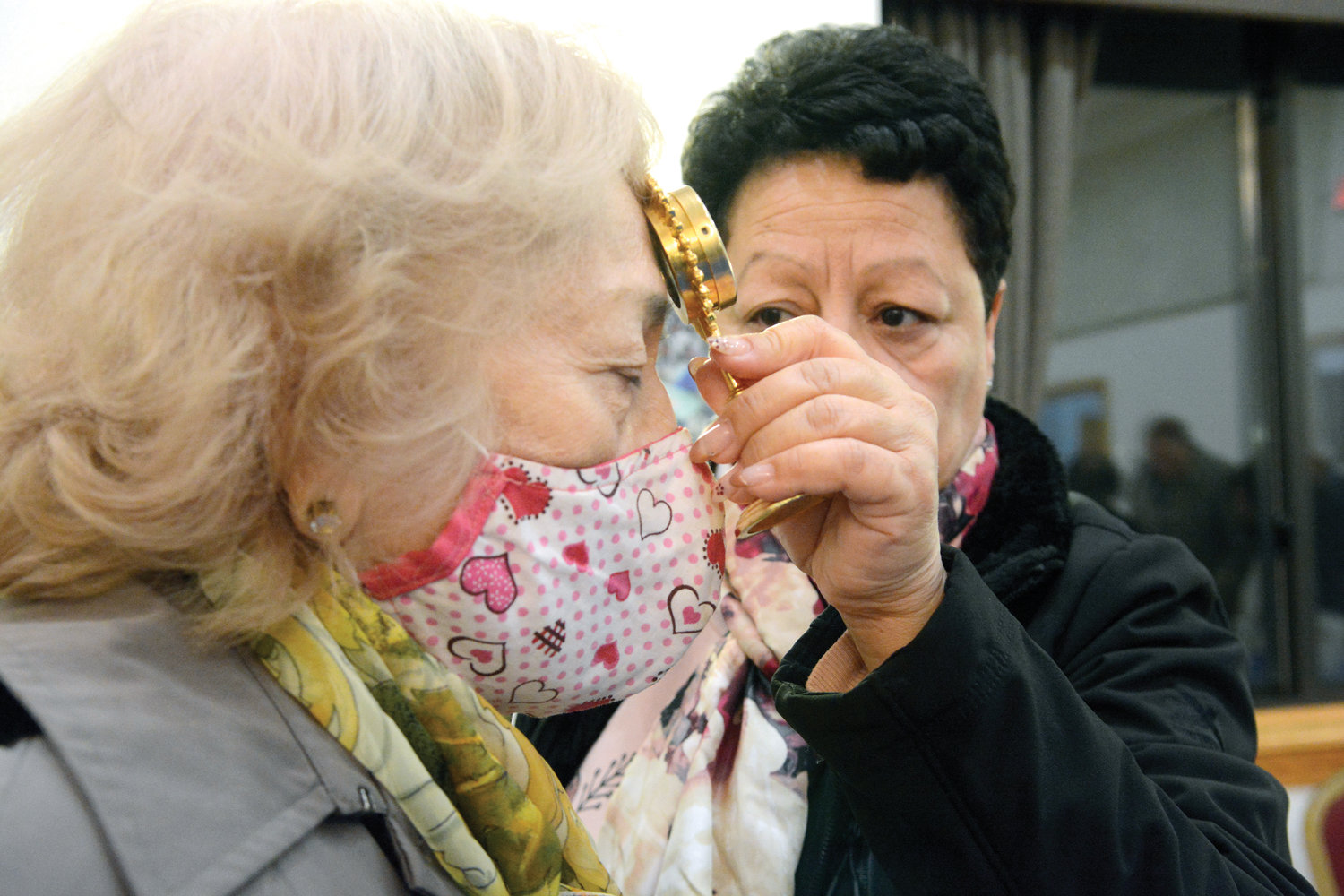 Agnes Davila holds a relic to Marcia Muros’ forehead. Both women are Eucharistic ministers at the shrine.