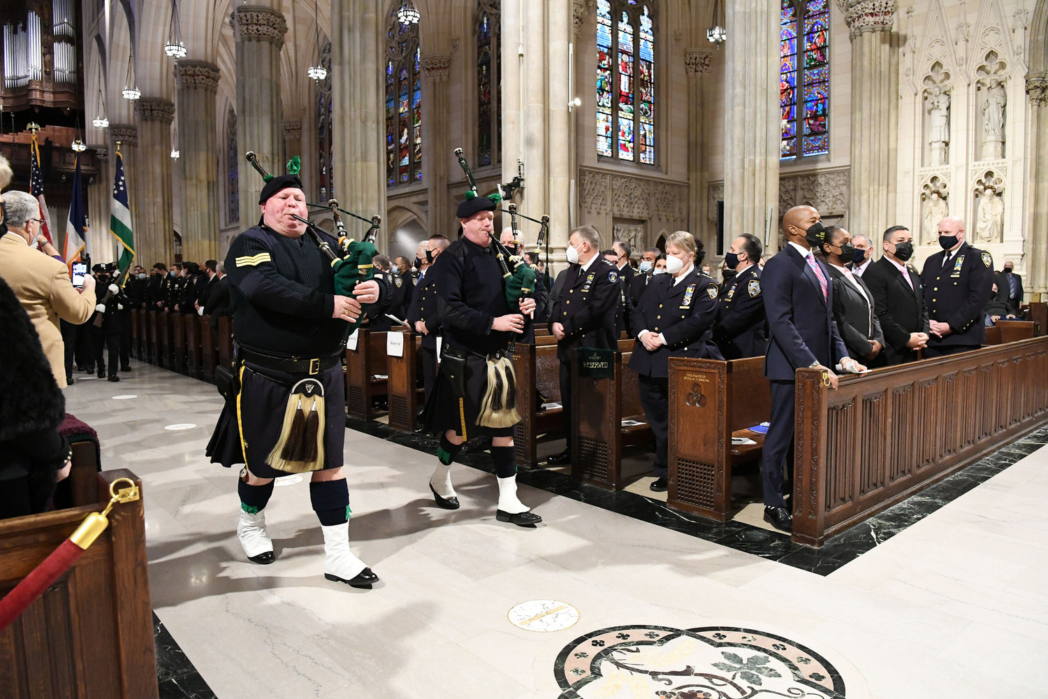 NYPD bagpipers lead the procession. In front pew at right are, from left, Mayor Eric Adams; NYPD Commissioner Keechant Sewell; Edward Caban, First Deputy Commissioner, NYPD; and Kenneth Corey, NYPD Chief of Department.