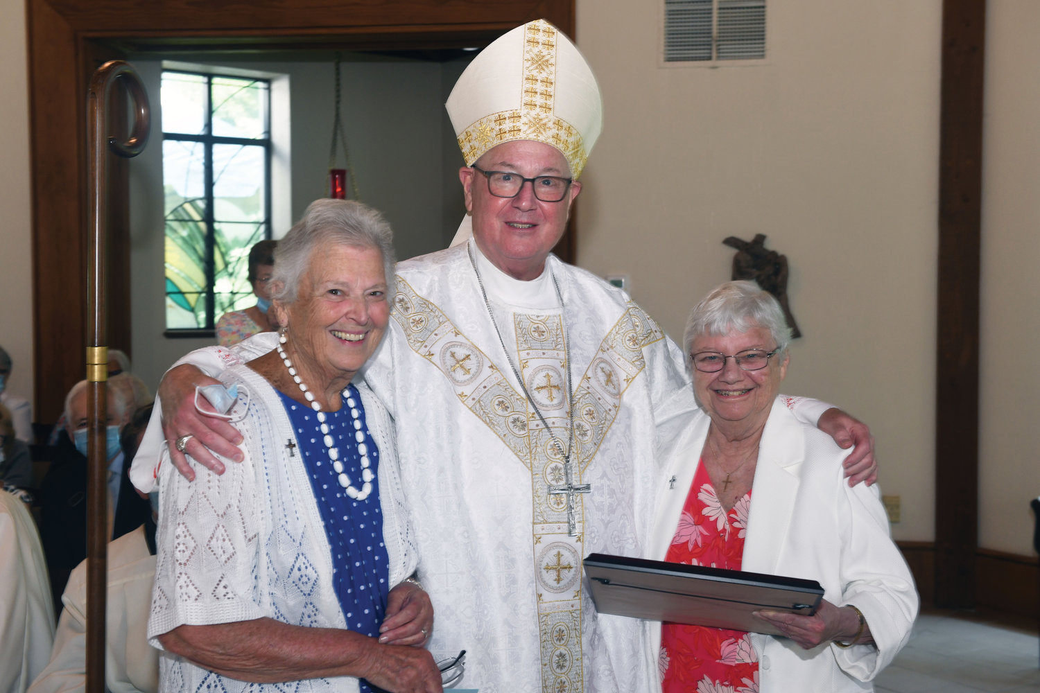 The cardinal and Sister Pat Vetrano, R.S.M., make a presentation to Sister Patricia Wolf, R.S.M., right, for her work in establishing Marian Woods.