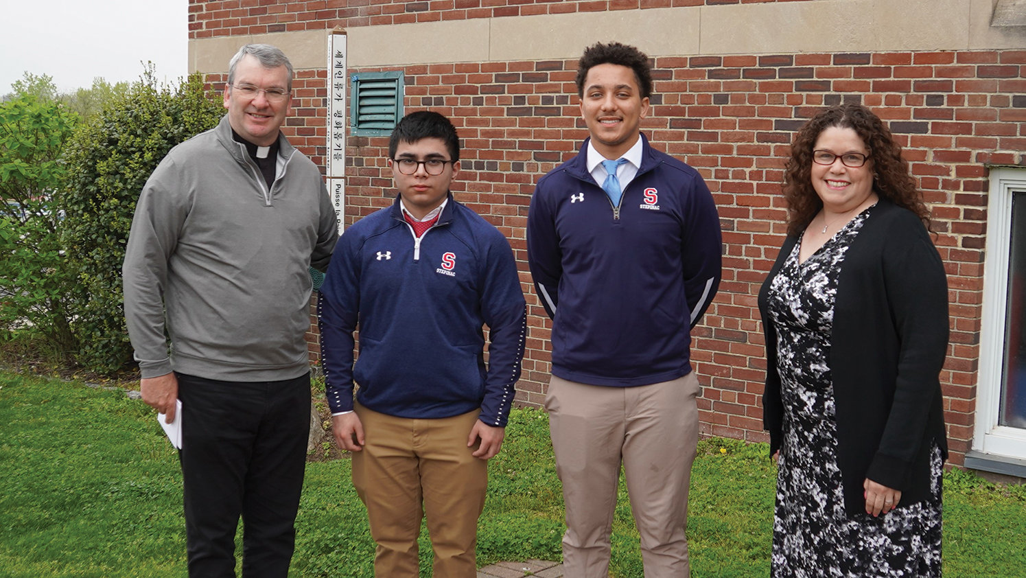 Father Thomas Collins, president of Archbishop Stepinac High School in White Plains, greets seniors Eduardo Ramirez and James McCauley, the recipients of the 2022 Xavier E. Flores Memorial Scholarship, and Evelyn Flores, his widow.