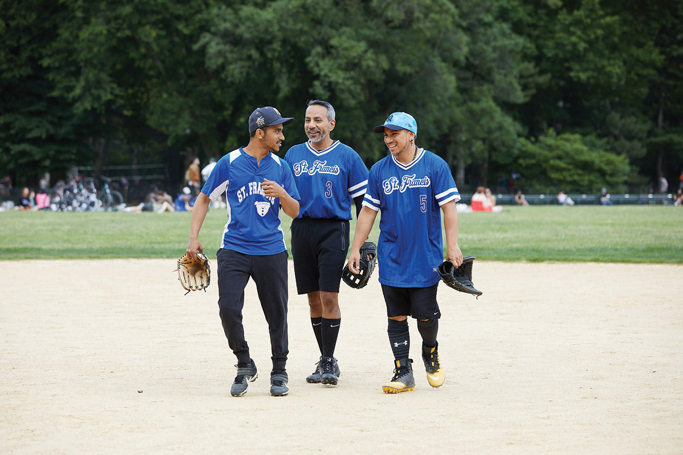 St. Francis players Johnathan Acosta, and brothers J.P. and Ken Garces, left to right, meet on the softball diamond during their team’s 5-2 win over Holy Name of Jesus in Central Park the same day.