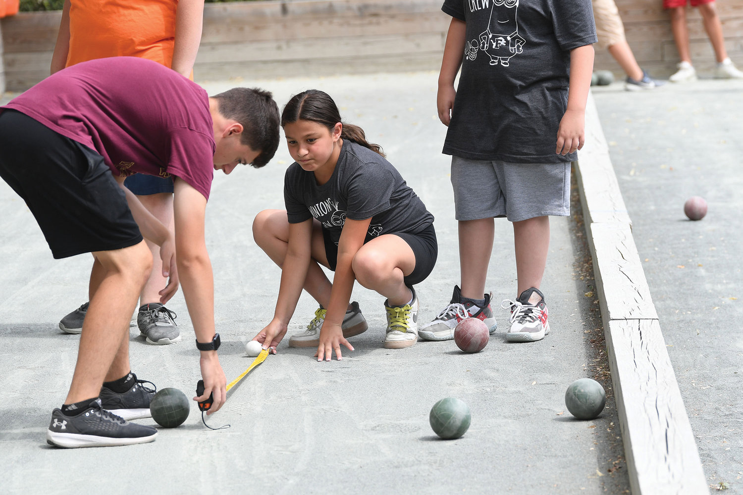 Joe Costa, Msgr. Farrell student and camp counselor, at left, assists as players measure the distance from the bocce ball to the pallino.